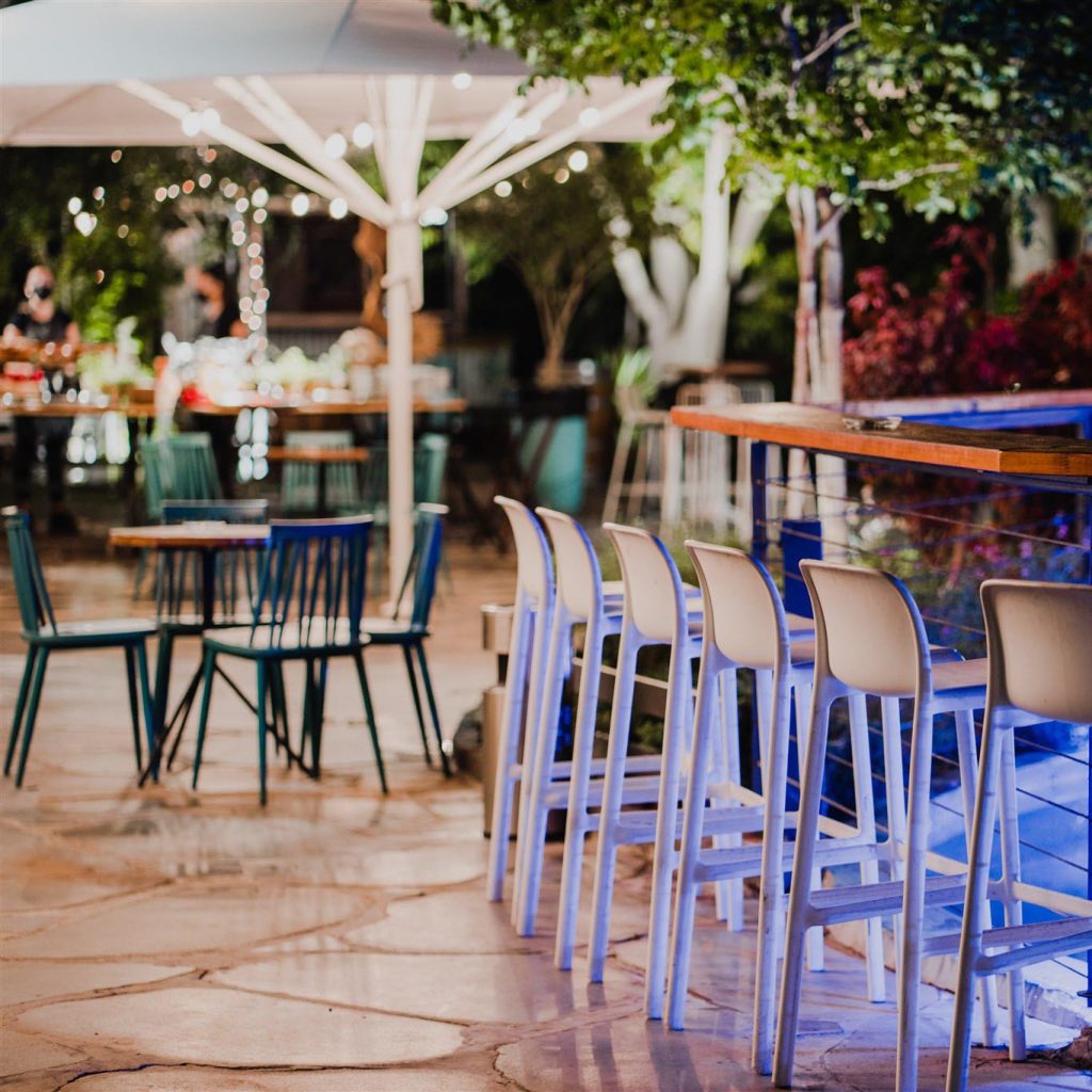 ישיבה בקבלת פנים בקיץ כסאות בר לבנים ליד בר עץ ופינות ישיבה ברקע