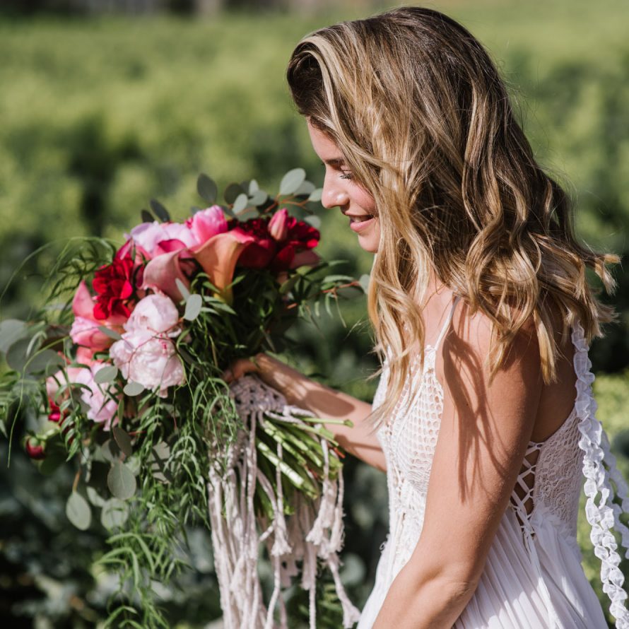 A bride in a field holding a large bouquet of red and pink flowers