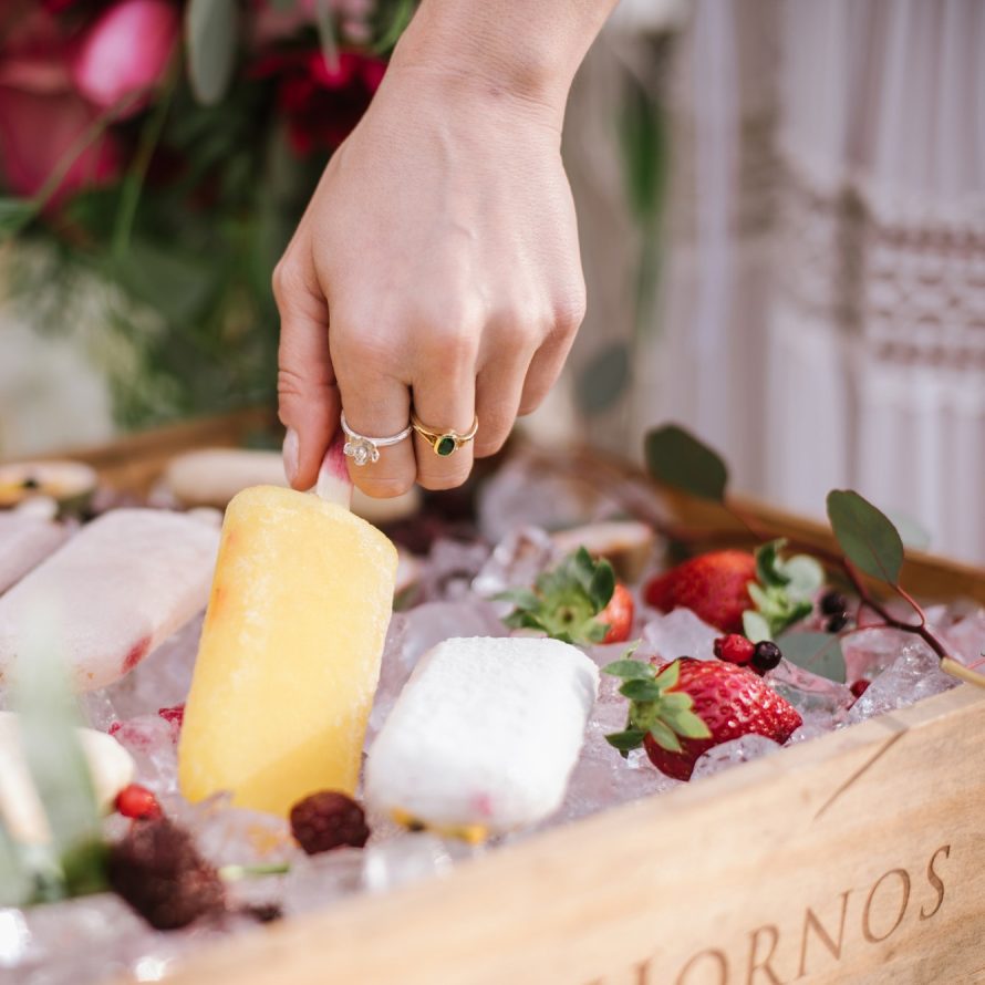 A hand takes a natural yellow popsicle from a wooden tray with ice
