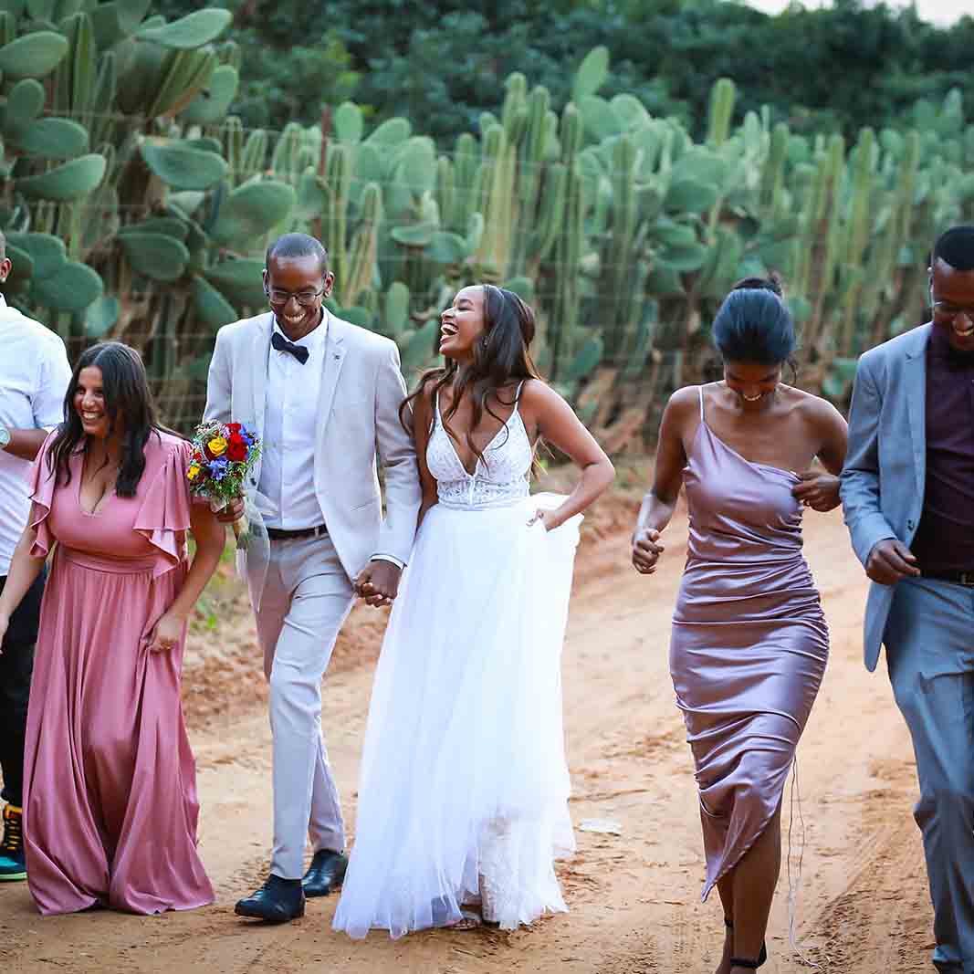 A bride and groom and their companions walk on a foot path next to a row of cacti