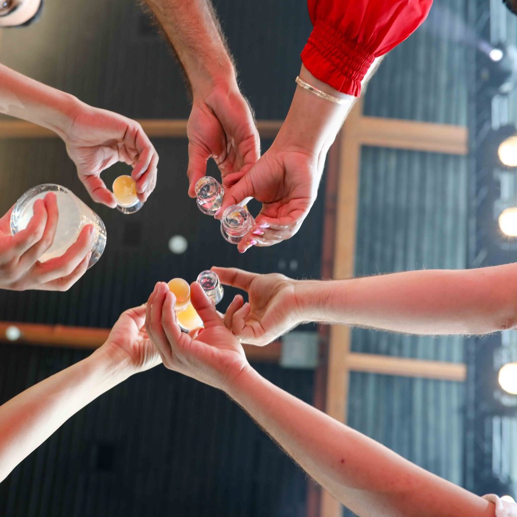 hands raise glasses of alcohol to cheer L’chaim