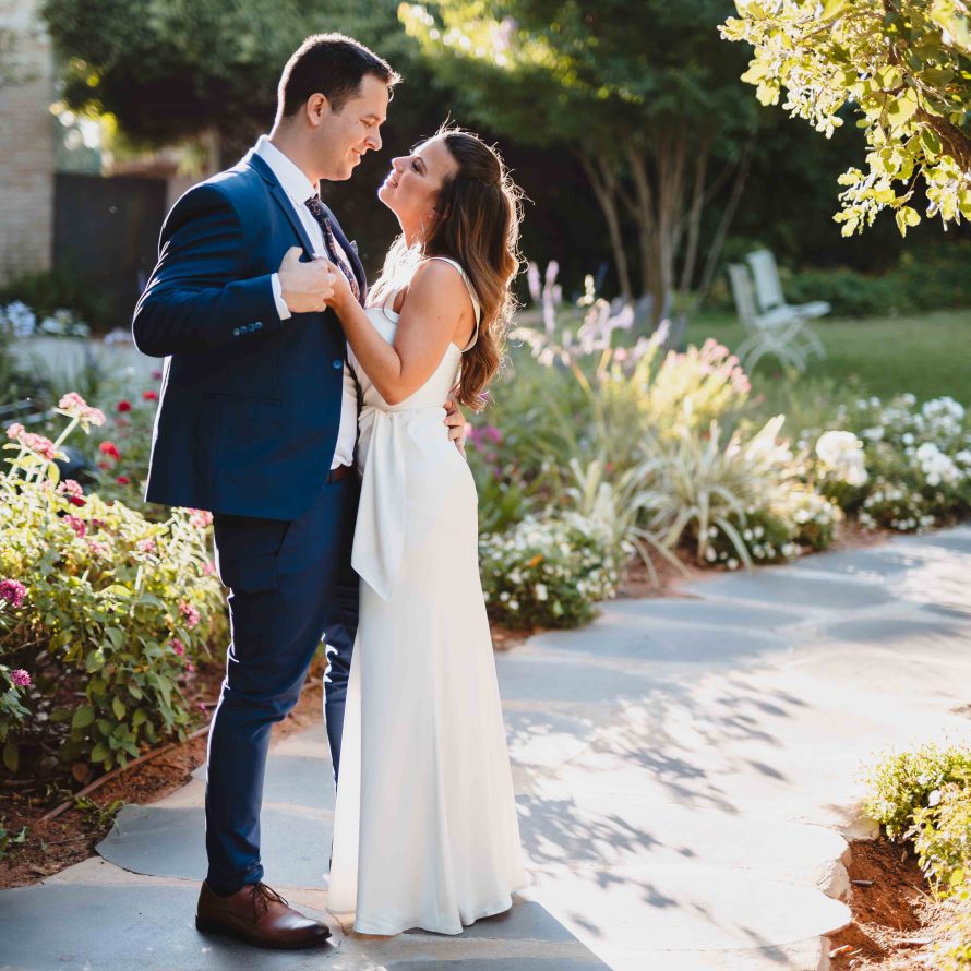 A bride and groom embrace and look into each other's eyes against the background of a blooming garden in the event garden