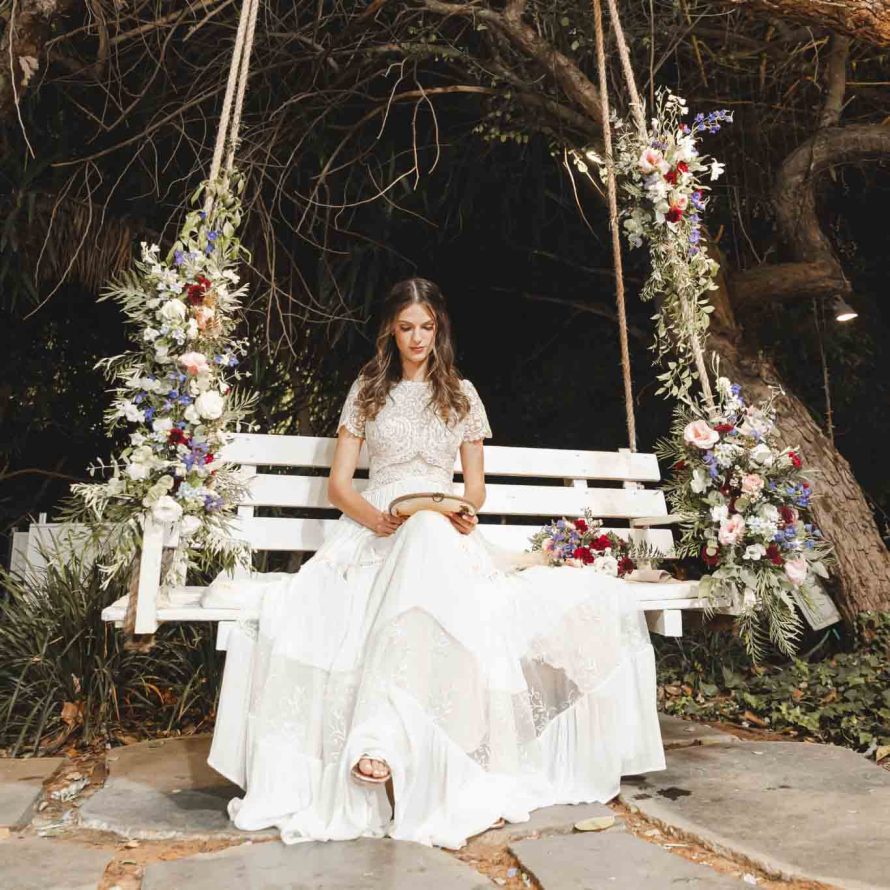 A bride sits on a white swing chair decorated with flowers in the weddings garden