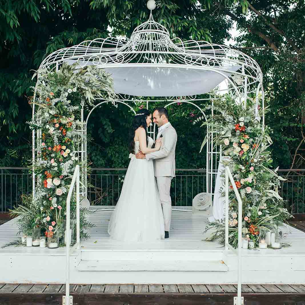 A couple under a gazebo canopy decorated with flowers and vegetation