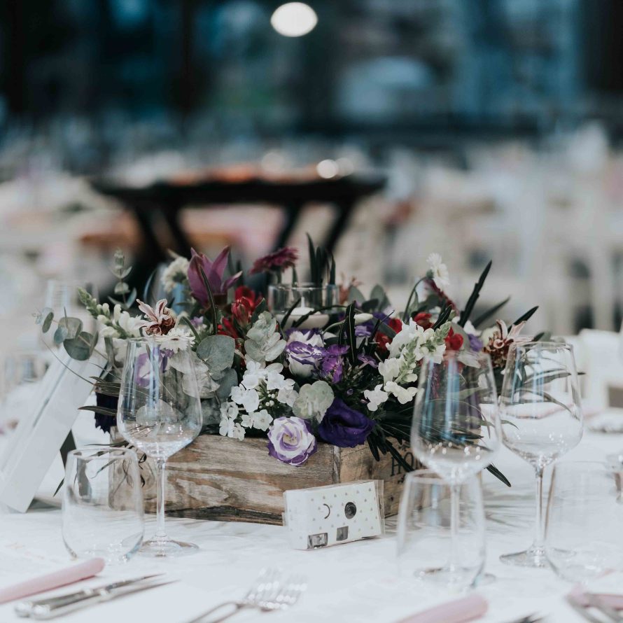 סידור פרחים בצבעי לבן, סגול, אדום וירוק על שולחן ערוך לחתונה