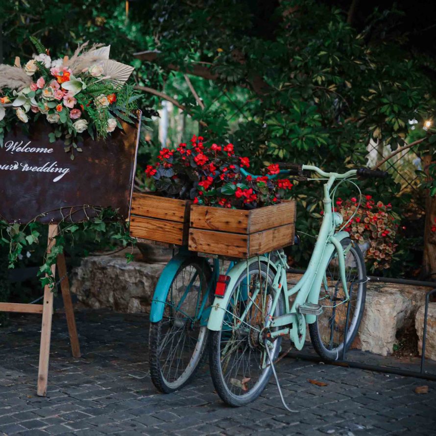 2 vintage bicycles with red flowers in wooden boxes next to a sign decorated with flowers