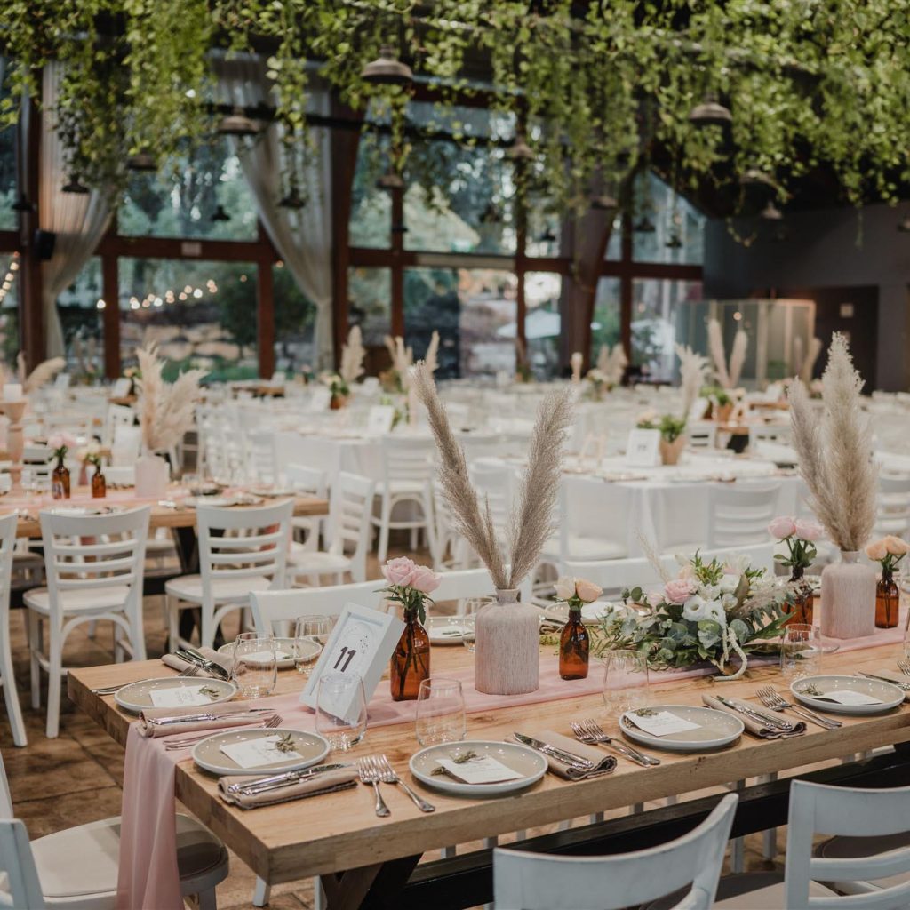 שולחן עץ ערוך ומעוצב עם ראנר ורוד, בקבוקים עם פרחים וסידורי פרחים