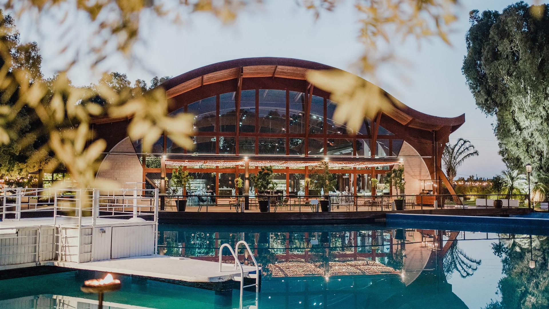 Transparent banquet hall with rounded roof reflected in a water pool