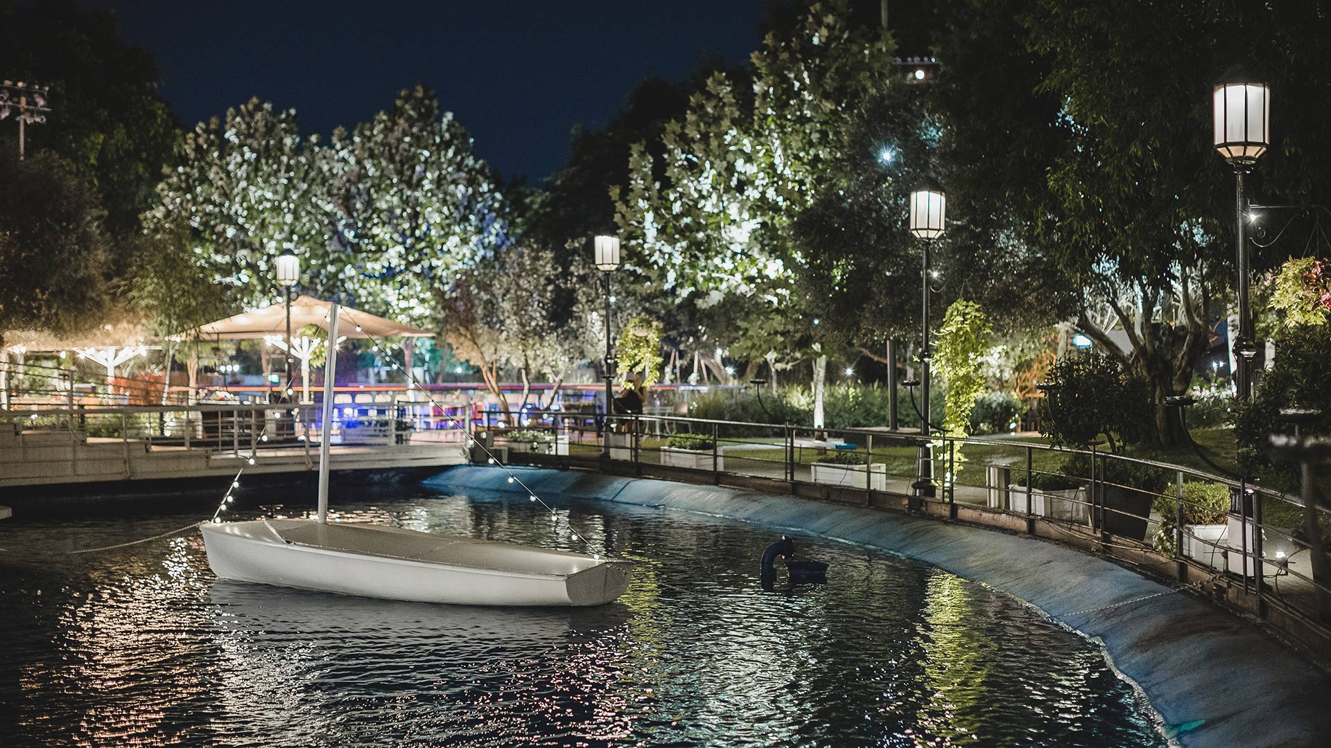 White boat lit up in a pool of water surrounded by lighting poles and illuminated trees