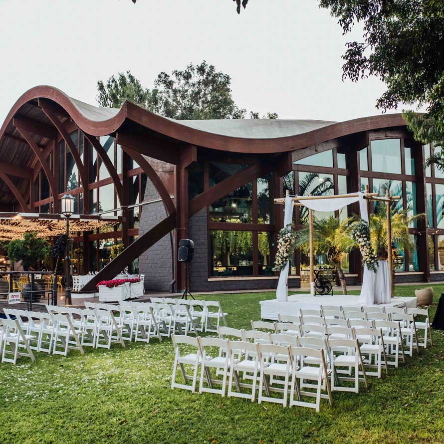 White wooden chairs in front of a bamboo canopy on the grass against the background of a transparent banquet hall