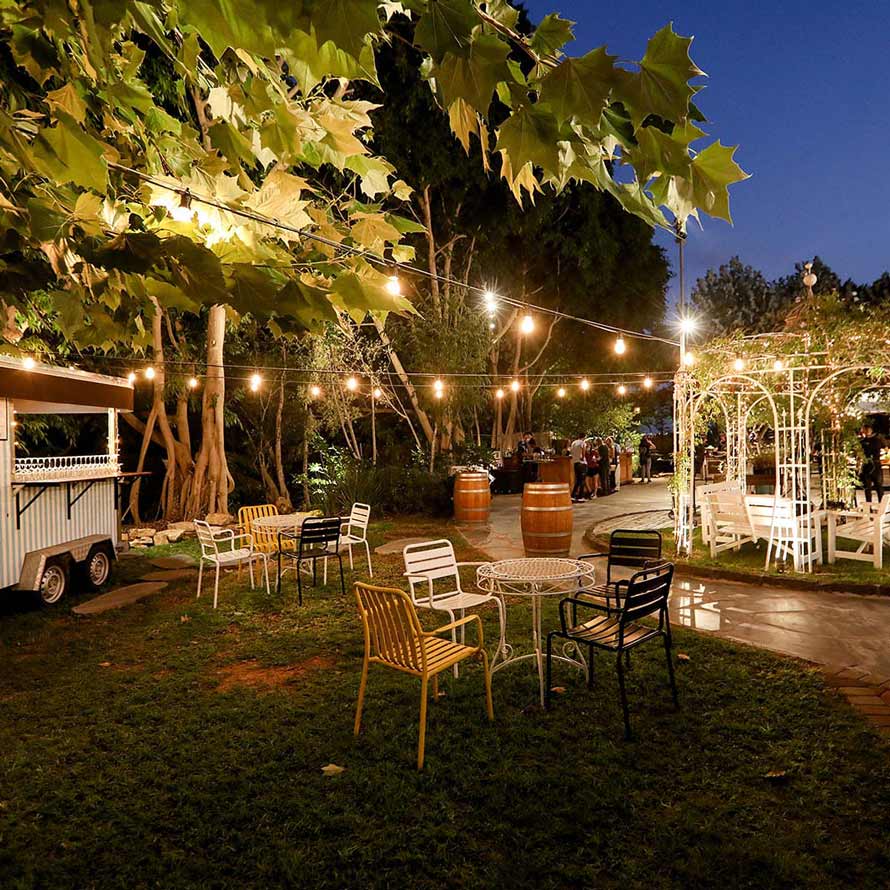 A wine bar cart and seating areas on the grass, a wine barrel and string lights lighting