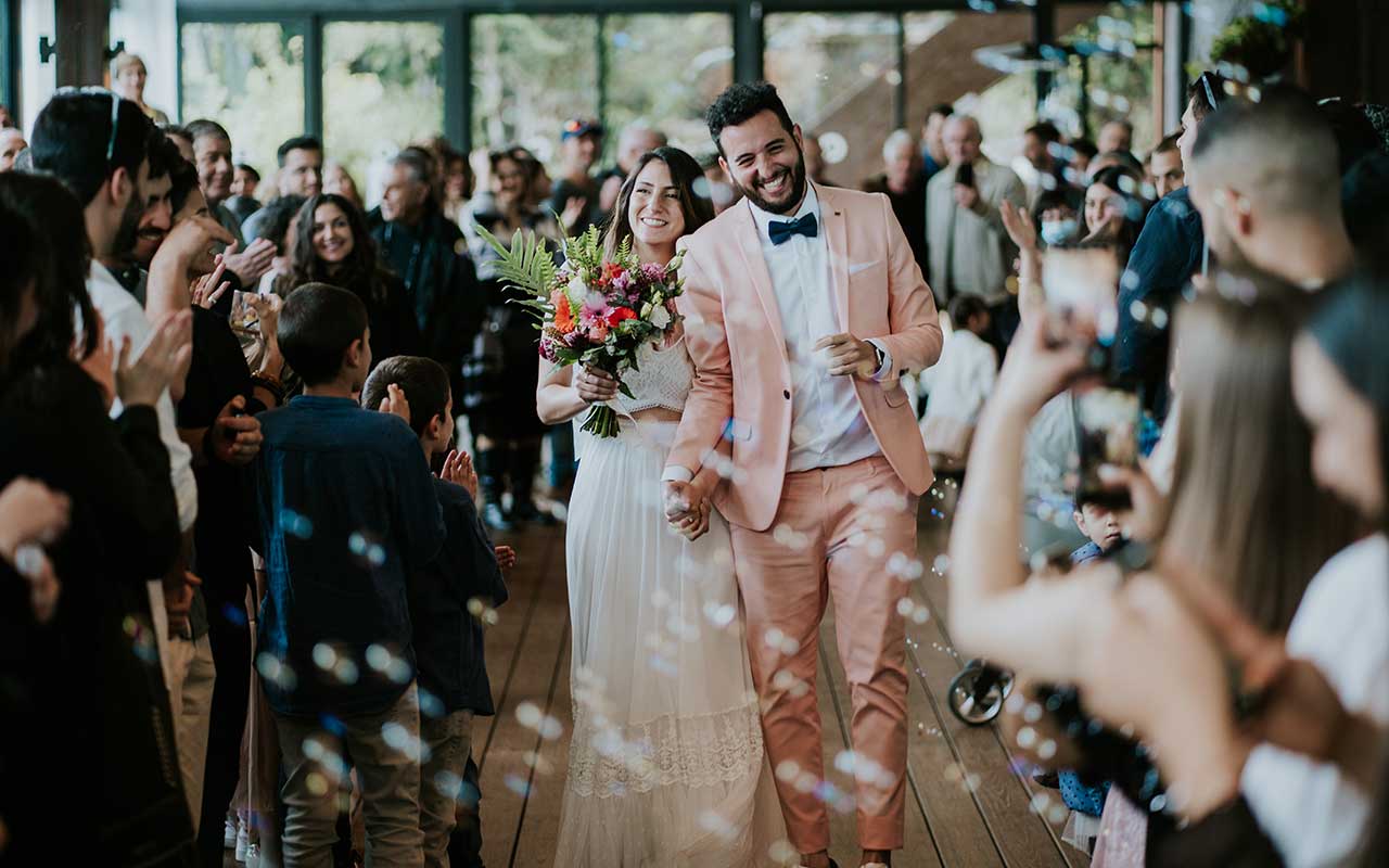 חתן וכלה מוקפים באורחים צועדים יד ביד