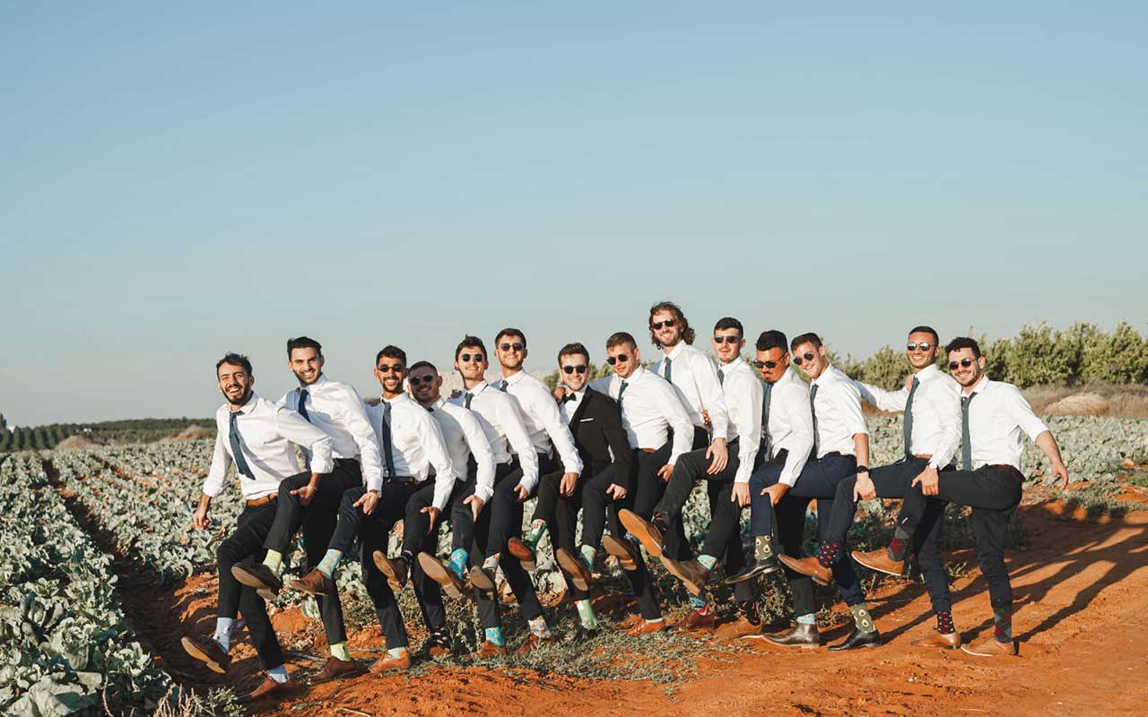 שורה של חתן ומלוויו חושפים גרביים צבעוניות בשדה כרוביות